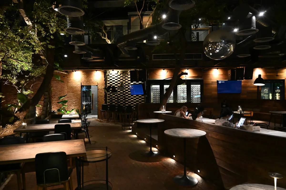 Terraza de un bar acogedor de noche, con mesas de madera y luces cálidas entre plantas